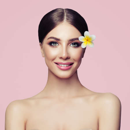 Facial treatment, cosmetology, beauty and spa. Smiling woman with perfect healthy skin and tropic flower on pink background. Facial treatment, cosmetology and spaの写真素材