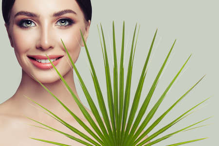 Happy smiling woman with healthy skin and green palm leaf on grey background. Facial treatment, cosmetology and spa beautyの写真素材