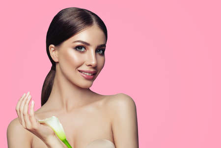 Young spa woman with healthy skin and white flowers on pink background. Facial treatment, cosmetology and spa treatmentの写真素材
