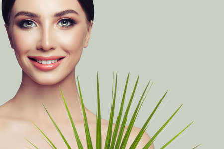 Attractive spa woman model with healthy skin, cute smile and green palm leaf. Facial treatment, cosmetology and spa beautyの写真素材