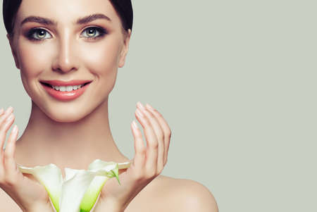 Female face closeup. Spa woman with healthy skin, manicured hands and white flowers. Facial treatment, cosmetology and spaの写真素材