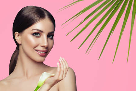 Beautiful young woman with healthy skin and white flowers on pink background. Facial treatment, cosmetology and spa treatmentの写真素材