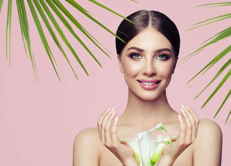 Perfect young woman smiling, spa portrait with tropic leaves and flowers on pink backgroundの写真素材