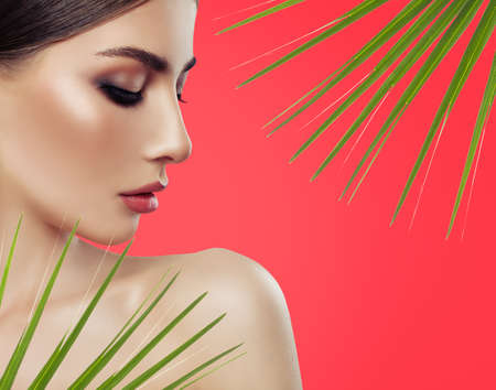 Beautiful young woman with green leaves, closeup portrait on red background. Facial treatment.の写真素材
