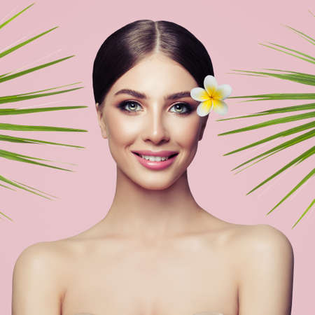 Beauty smiling spa model with natural make up and green leaves on pink background. Spa and wellness. Skin care conceptの写真素材