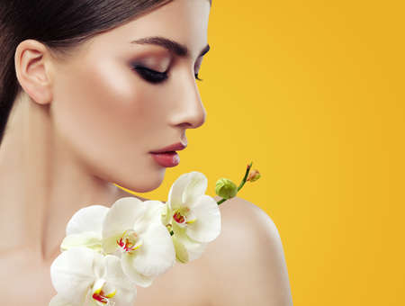 Young Perfect Woman Face with Makeup and Orchid Flowers on Bright Yellow Background, Beauty Portraitの写真素材