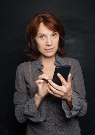 Business woman with smartphone texting coworker. Mid adult business woman cell phoneの写真素材