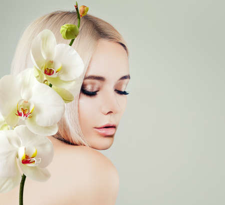 Young woman face closeup. Spa model with clean skin and white orchid flowers. Facial treatment, cosmetology, beauty salon, skin care and spa backgroundの写真素材