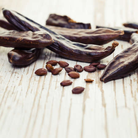 Carob. Healthy organic sweet carob pods and seeds on white wooden background closeup.の写真素材