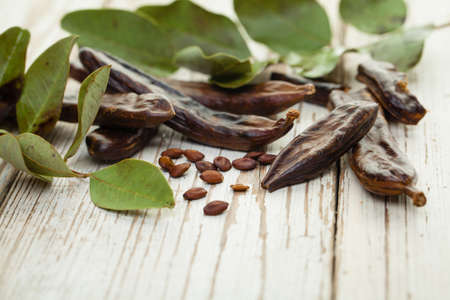 Carob. Healthy organic sweet carob pods with seeds and green leaves on a wooden board. Healthy eating, food background.の写真素材