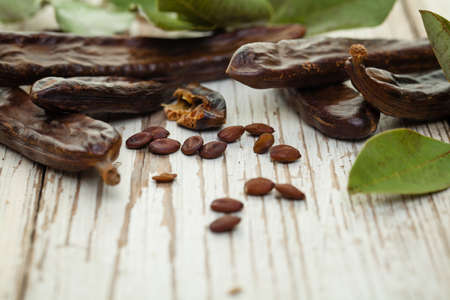 Carob. Organic carob pods with seeds and leaves on white wooden table. Healthy eating, food...