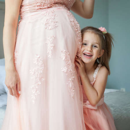 Happy daughter and pregnant mother. Little child girl and pregnant bellyの写真素材