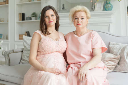 Beautiful senior mom and her adult daughter are hugging, looking at camera and smilingの写真素材