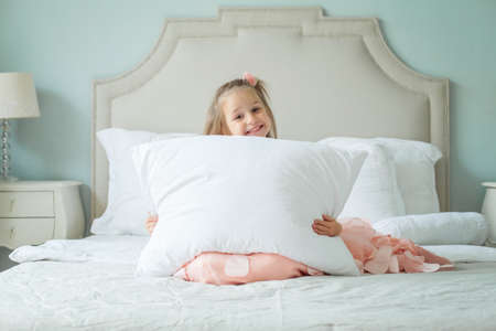 Happy child girl with white pillow at homeの写真素材