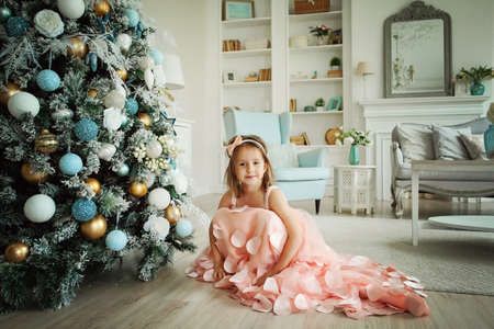 Smiling child girl with Christmas tree at homeの写真素材
