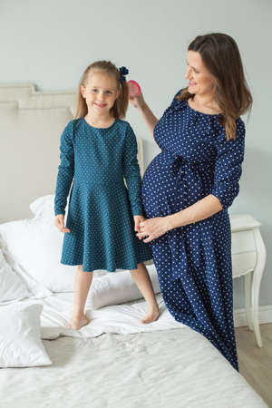 Happy family. Pregnant mother and little daughter. Mother combing child girlの写真素材