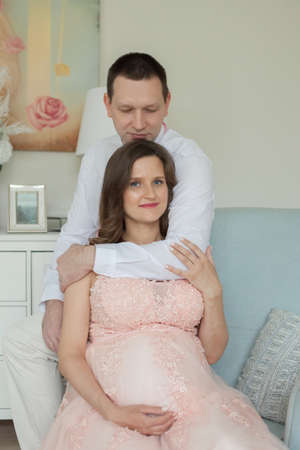 Pregnancy and people concept - happy man hugging his pregnant wife at homeの写真素材