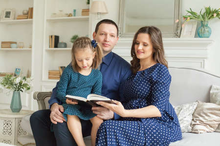 Happy family. Mother, father and child daughter reading a book together at home.の写真素材