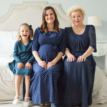Laughing mother, daughter, grandmother. Senior woman, pregnant adult woman and child girl at home. Happy female generation.の写真素材