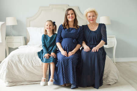 Happy family. Mother, daughter, grandmother. Older woman, pregnant adult woman and child girlの写真素材