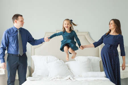 Happy family jumping on the bed. Mother, father daughter having fun. Parental care concept.の写真素材
