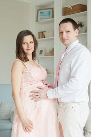 Happy man touching belly of smiling pregnant woman at homeの写真素材