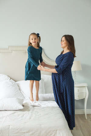 Happy family. Pregnant mother and little daughter jumping on the bedの写真素材