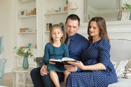 Happy family at home. Mother, father and child daughter reading a book togetherの写真素材