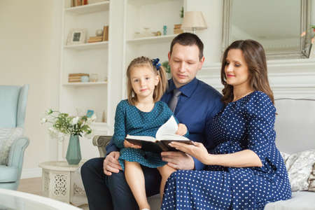 Family at home. Mother, father and child daughter reading a book togetherの写真素材