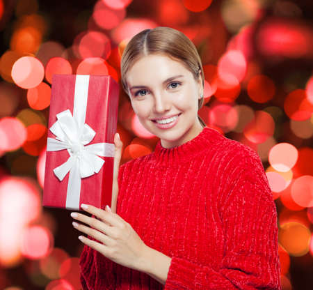 Smiling woman in sweater with red gift box on bokeh backgroundの写真素材