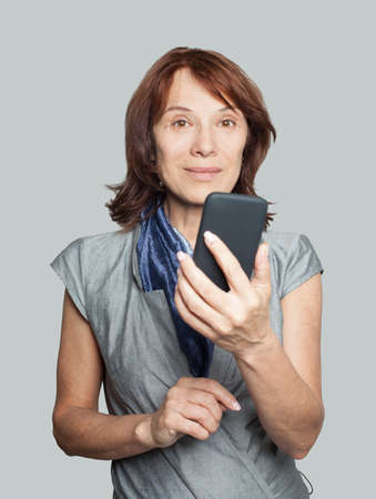 Mature woman smiling, using smartphone and chatting, portraitの写真素材