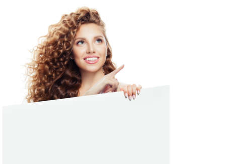 Happy woman pointing up and holding white empty paper boardの写真素材