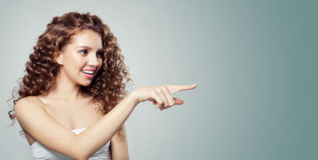 Pretty woman pointing and showing empty copy space. Beautiful girl with long curly hair pointing to the side. Presenting your product. Positive emotion. Expressive facial expressionsの写真素材