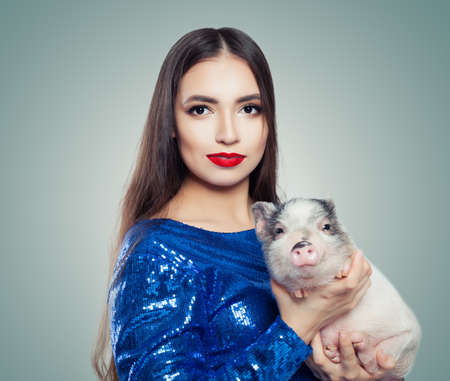 Beautiful brunette woman in blue glitter dress holding little pigの写真素材