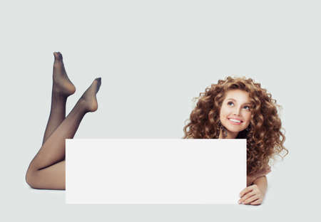 Young happy woman in black tights lying on white and showing big empty paper card bannerの写真素材