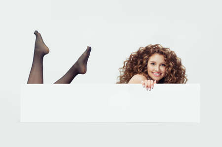 Glamorous female model woman in black tights lying on white  and showing big white empty paper card banner with copy spaceの写真素材
