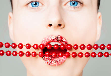 Creative portrait of woman face with closeup bright lips and red pearls. Perfect female mouth with glitter lipstick makeup の写真素材
