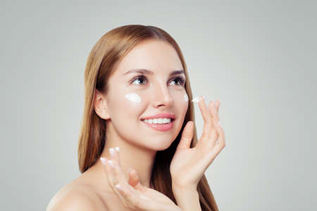 Healthy young woman with clear skin applying moisturizing cream on whiteの写真素材