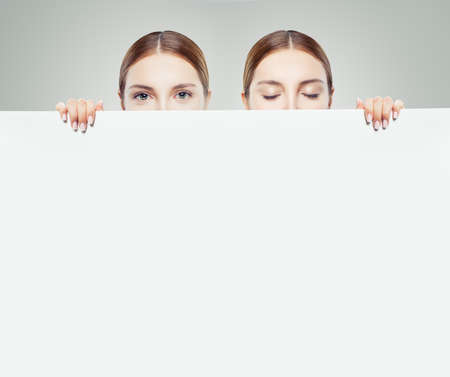 Two young women looking up and down and showing white empty paper card background with copy space for advertising marketing or product placementの写真素材