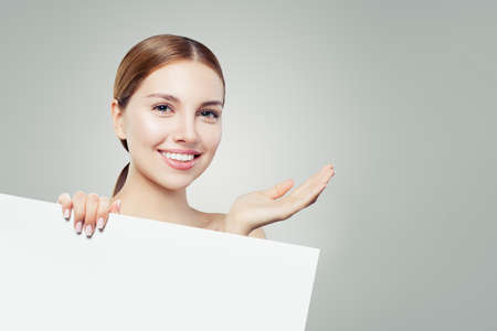 Young perfect girl laughing and showing empty open hand and white paper banner board background for advertising marketing or product placementの写真素材