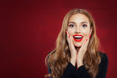 Young happy woman against red wall background. Surprised girl portrait. Positive emotions, facial expressionの写真素材