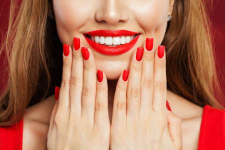 Perfect woman touching her face her hand with manicure. Makeup lips with red lipstick and red nail polish, beauty salon conceptの写真素材