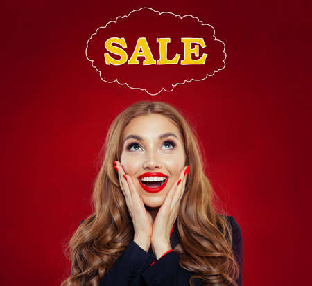 Sale concept with happy surprised woman on red background. Beautiful girl with red lips makeup and long curly hairstyle portraitの写真素材