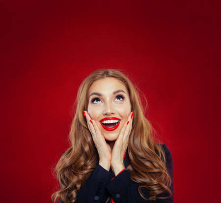 Happy surprised woman looking up on red background. Positive emotions, facial expressionの写真素材