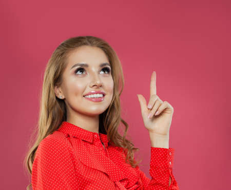 Portrait of happy young woman pointing up her finger on bright colorful pink background. Student girl pointing fingerの写真素材