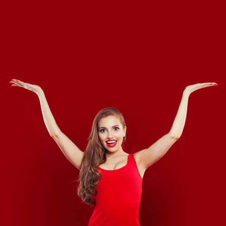 Happy excited surprised woman in red dress having fun on red colorful bright background. Girl with empty hands up. Positive emotion. Expressive facial expressionの写真素材