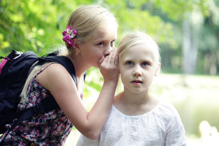 Two Sister Girls Whisper In Ear outdoors. Concept of joke, secret, fantasy, conversation, whisper....