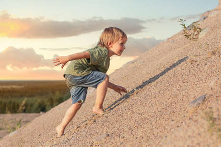 Boy Climbing On Mountain. Summer day and sand dune.の写真素材