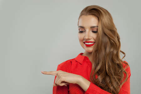 Attractive model with makeup and long curly hair pointing aside and smiling on white backgroundの写真素材