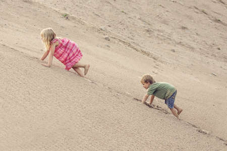 Girl and boy Climbing On The Sand dune. Summer dayの写真素材